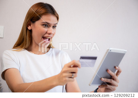 Happy young caucasian woman holding credit card or debit card paying with shopping online. 129209212