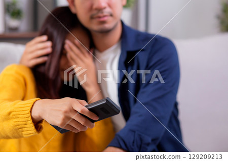 Closeup young asian couple watching a scary or thrilling TV show in living room. 129209213