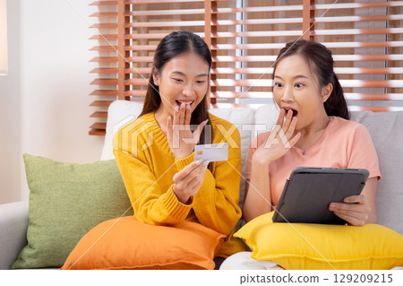 Two young asian woman sitting on sofa using tablet computer shopping online with credit card. Two young asian woman sitting on sofa using tablet computer shopping online with credit card. 129209215