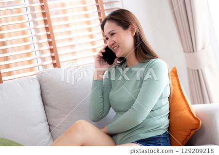 Young asian businesswoman telephone smiling and relax sitting on sofa in living room at home. Young asian businesswoman telephone smiling and relax sitting on sofa in living room at home. 129209218