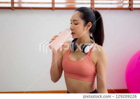Young asian woman in sportswear drinking water in bottle after workout and exercise in living room. Young asian woman in sportswear drinking water in bottle after workout and exercise in living room. 129209226