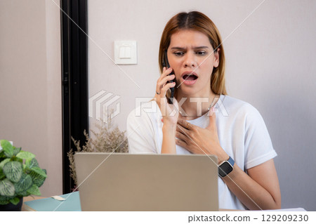 Young caucasian businesswoman working on laptop computer while talking on smartphone with stress. Young caucasian businesswoman working on laptop computer while talking on smartphone with stress. 129209230