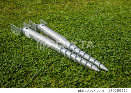 Metal Ground Screws for Foundation Anchoring on Green Grass 129209311
