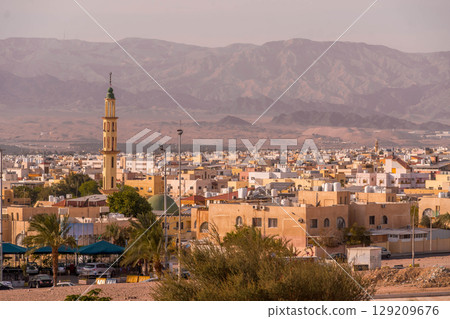 Panorama of Aqaba, a large Jordanian port city on the Red Sea, with a mosque minaret and colorful buildings set against the Israeli mountains at sunset. Panorama of Aqaba, a large Jordanian port city on the Red Sea, with a mosque minaret and colorful buildings set against the Israeli mountains at sunset. 129209676
