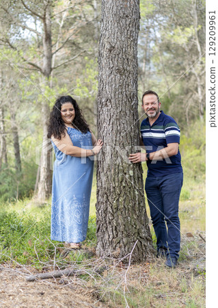 A man and woman are posing for a picture in front of a tree A man and woman are posing for a picture in front of a tree 129209961