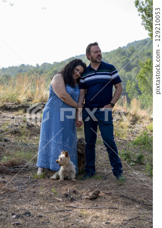 A man and woman are standing in a field with a dog 129210053