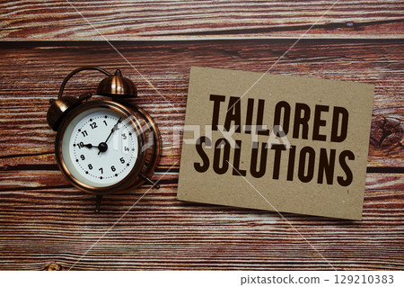 Tailored Solutions text with alarm clock on wooden background Tailored Solutions text with alarm clock on wooden background 129210383