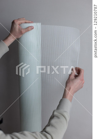 Male hands holding a roll of white plaster mesh for preparatory and painting works. 129210787