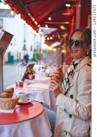 Stylish woman enjoys croissant and coffee at outdoor French cafe table 129211072