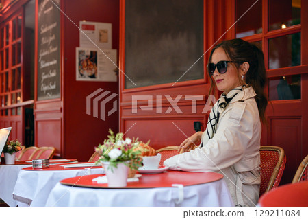 Elegant woman enjoying coffee alone at red French cafe terrace Elegant woman enjoying coffee alone at red French cafe terrace 129211084