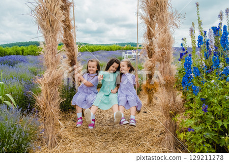 The twins are holding the ropes of a large swing tightly, and the older sister is sitting in the middle on a beautiful swing The twins are holding the ropes of a large swing tightly, and the older sister is sitting in the middle on a beautiful swing 129211278