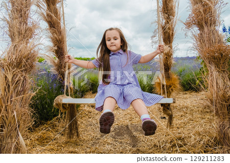 The girl is swinging on a swing among delicate lavender flowers The girl is swinging on a swing among delicate lavender flowers 129211283