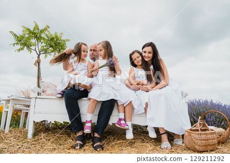 The family sits on a wooden bench among the purple lavender flowers The family sits on a wooden bench among the purple lavender flowers 129211292