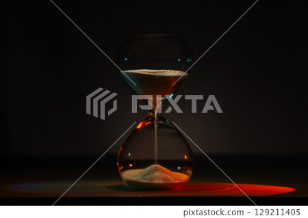artistic glowing neon hourglass, symbolizing time and creativity. Vibrant lighting against a dark minimalist backdrop. Concepts of time management, life balance, and artistic design. 129211405
