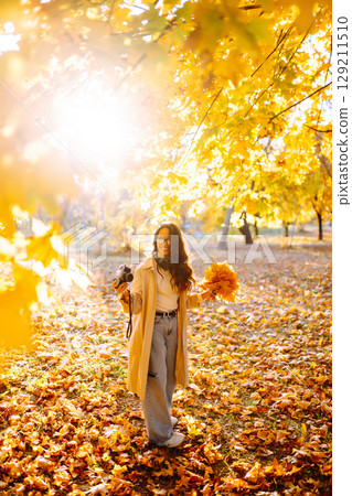 Young woman taking pictures in the autumn forest. Lady Walking In Fall Park With Yellow Foliage. 129211510