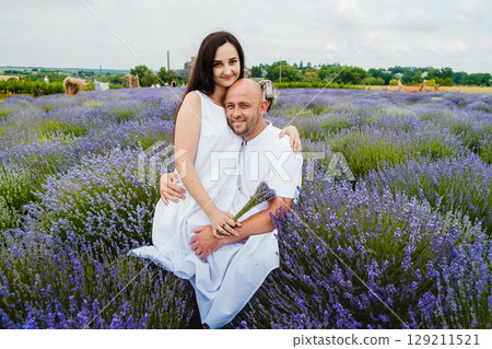 The man in a white T-shirt embraces his wife, who is sitting on his lap in the lavender field The man in a white T-shirt embraces his wife, who is sitting on his lap in the lavender field 129211521