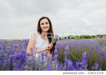 A young woman has sat down in the middle of a lavender field A young woman has sat down in the middle of a lavender field 129211529