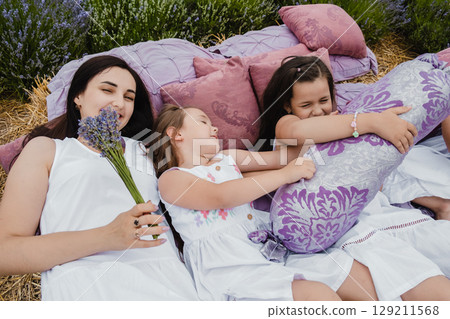 The mother and her daughters lie on a bed covered with a purple blanket, in the center of the lavender field The mother and her daughters lie on a bed covered with a purple blanket, in the center of the lavender field 129211568