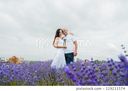 The lavender field envelops the lovers with a delicate scent, they stand in each other's arms The lavender field envelops the lovers with a delicate scent, they stand in each other's arms 129211574