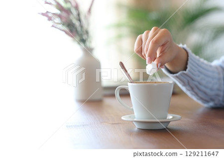 Woman hand throwing sugar in a coffee cup at home 129211647