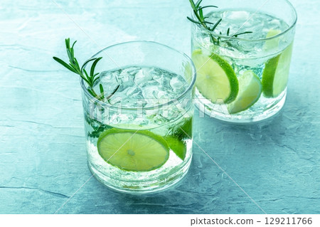 Gin tonic, two glasses of gin with soda, lime, rosemary, and ice, on blue 129211766