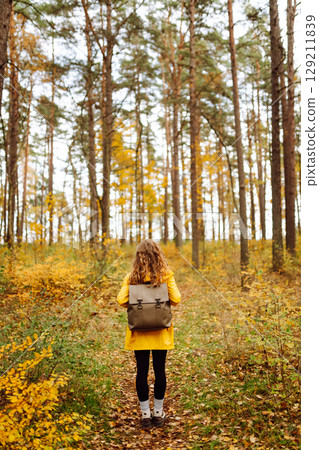 Back view. Curly woman with backpack in autumn forest enjoying nature. Concept of relaxation, nature 129211839