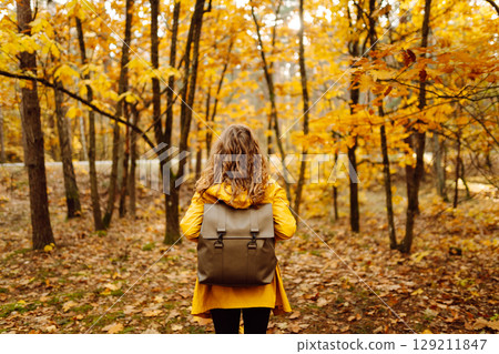 Back view. Curly woman with backpack in autumn forest enjoying nature. Concept of relaxation, nature Back view. Curly woman with backpack in autumn forest enjoying nature. Concept of relaxation, nature 129211847