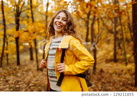 Hiking in autumn forest. Smiling tourist in bright coat walks through autumn park in sunny weather. Hiking in autumn forest. Smiling tourist in bright coat walks through autumn park in sunny weather. 129211855