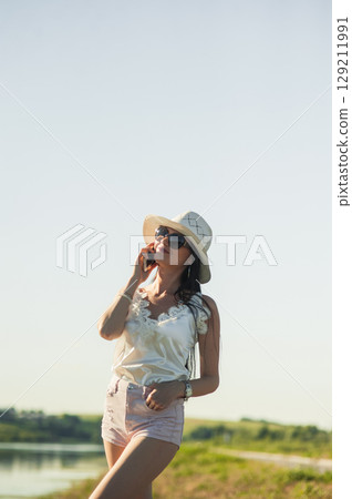 A girl in white is talking on the phone with concentration near the lake surface 129211991