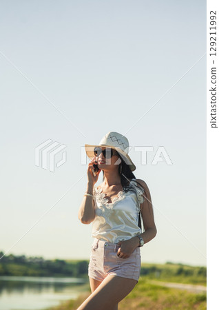 A young lady in light summer clothes stands by the lake 129211992