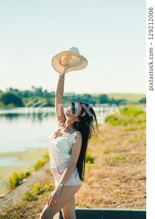 A slender girl in white raises her hat up with a smile, as if catching the wind 129212006