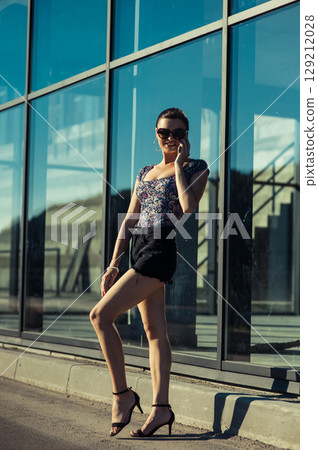 A young girl stands in the sunlight, holding her phone to her ear 129212028