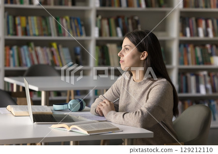 Pensive confident teen female student visualizing idea at library table Pensive confident teen female student visualizing idea at library table 129212110
