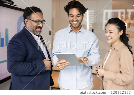 Smiling businesspeople of different ages ethnicities looking on tablet screen Smiling businesspeople of different ages ethnicities looking on tablet screen 129212132