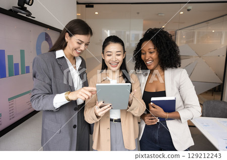 Multiethnic young businesswomen having fun together looking at tablet pc 129212243