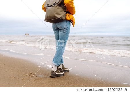 Close-up of woman's legs in boots. Tourist walk along beach near sea. Adventure, vacation concept. 129212249
