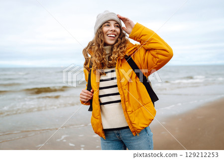 A beautiful young tourist woman in a yellow jacket with a backpack enjoys life near the sea. Travel. A beautiful young tourist woman in a yellow jacket with a backpack enjoys life near the sea. Travel. 129212253