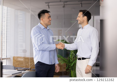 Two multiethnic businessmen shaking hands in modern office Two multiethnic businessmen shaking hands in modern office 129212282