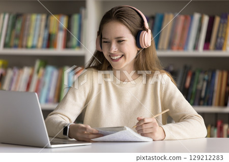 Teen girl student wearing earphones learning on distance via notebook 129212283