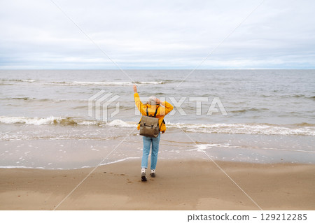 Attractive woman on windy cold beach. Beautiful tourist woman in stylish clothes enjoys life by sea. 129212285