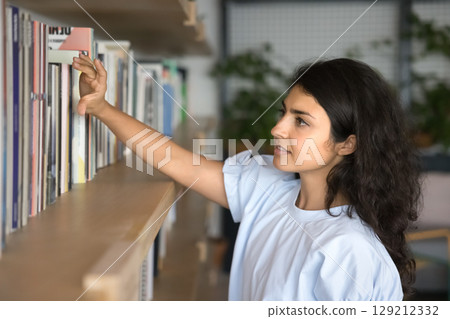 Young student woman browsing through books in library Young student woman browsing through books in library 129212332