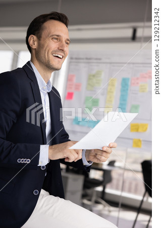 Professional man holding documents looks into distance with contented smile Professional man holding documents looks into distance with contented smile 129212342