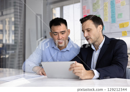 Two professional men looking at tablet screen seated at table 129212344