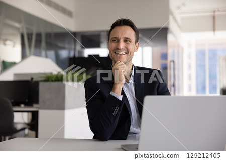 Positive middle-aged 40s man sits in workplace with laptop Positive middle-aged 40s man sits in workplace with laptop 129212405