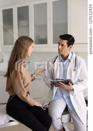 Serious physician man in lab coat listening to female patient 129212424