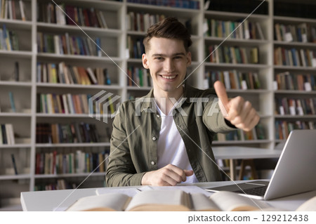 Smiling male student sitting at classroom desk showing thumbs up 129212438