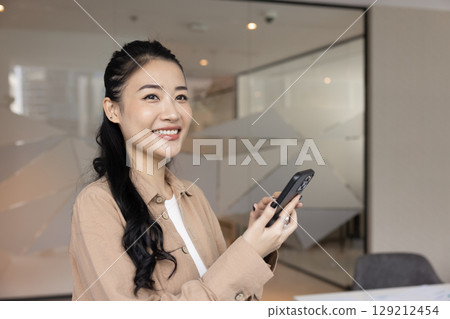 Beautiful female office worker using mobile phone app in office 129212454