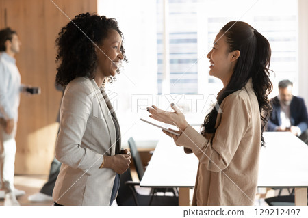 Young multiracial businesswomen colleagues laugh chat in modern office Young multiracial businesswomen colleagues laugh chat in modern office 129212497