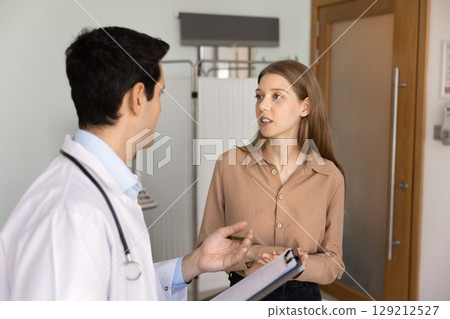 Serious young 20s patient woman talking to male doctor 129212527