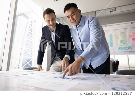 Two diverse teammates analyzing printed graphs and charts 129212537